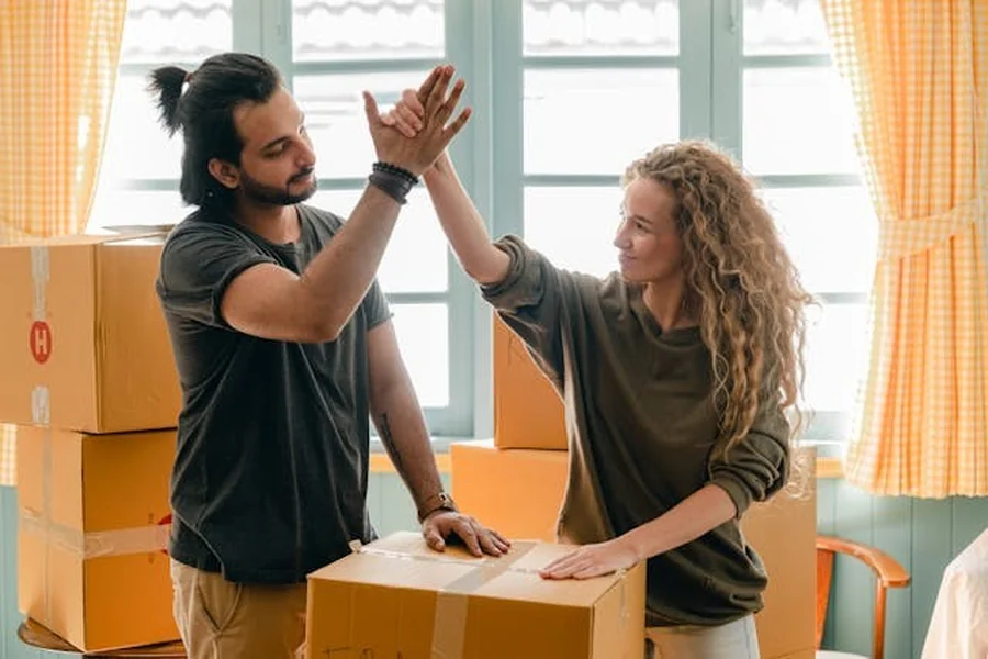 A man and a woman giving each other a high-five while standing next to cardboard boxes